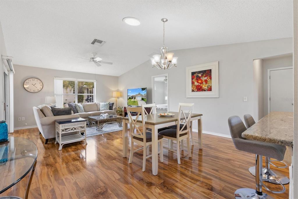 A living and dining area features hardwood floors, a vaulted ceiling, and a kitchen island — 3443 SIPSEY STREET, THE VILLAGES, FL
