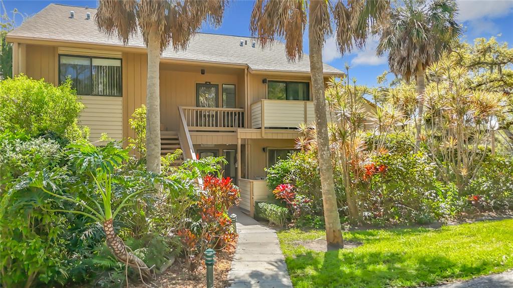 A two-story tan apartment building features a wooden staircase leading to an upper balcony — 1617 BROOKHOUSE DRIVE UNIT BR260, SARASOTA, FL