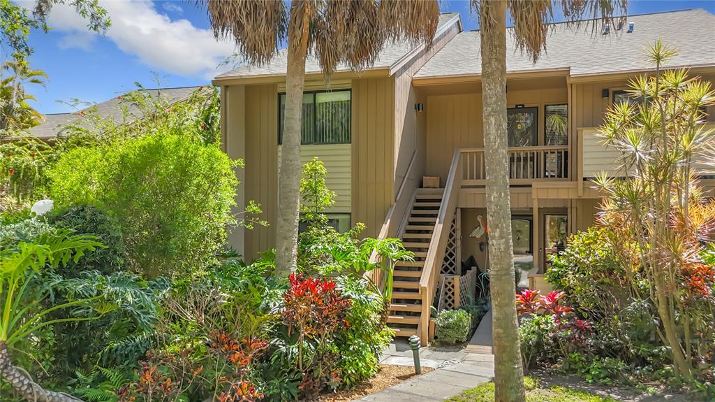 An exterior view of a two-story tan building with wooden stairs and lush landscaping — 1617 BROOKHOUSE DRIVE UNIT BR260, SARASOTA, FL
