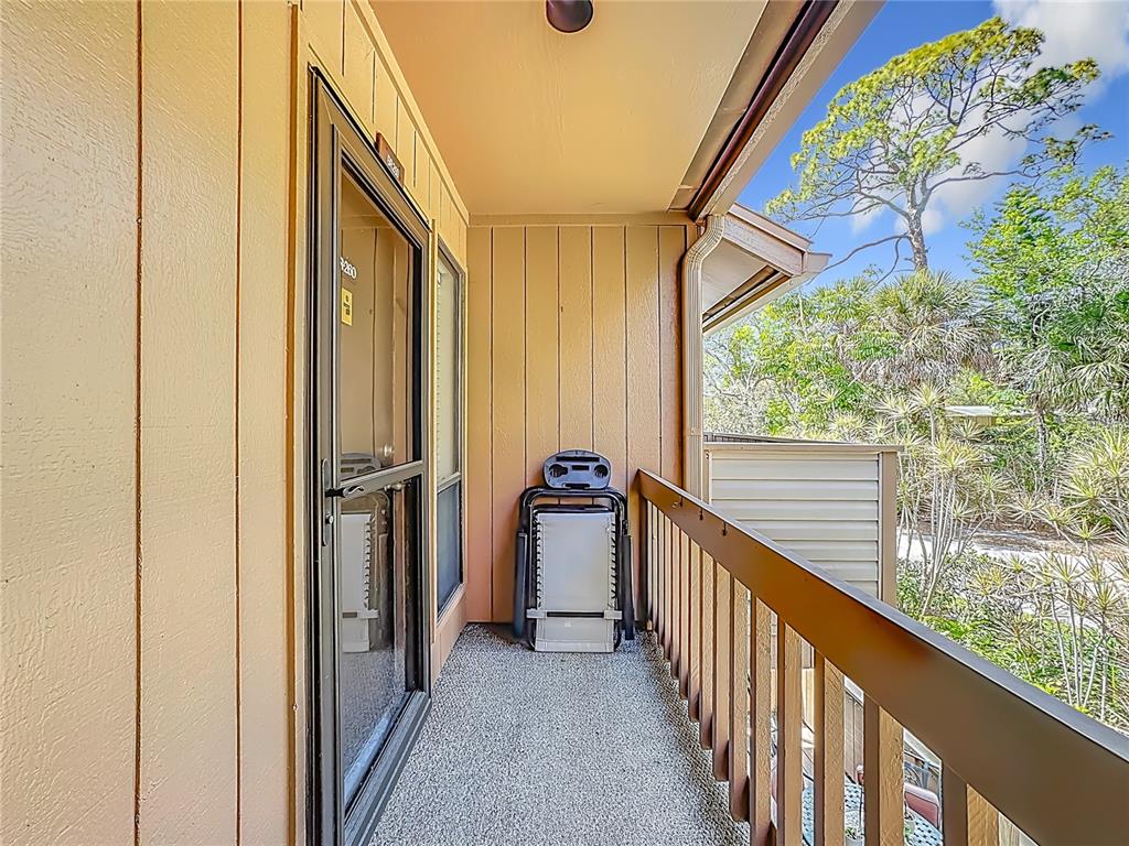 A balcony with a textured floor, wooden railing, and a folded chair against the wall — 1617 BROOKHOUSE DRIVE UNIT BR260, SARASOTA, FL