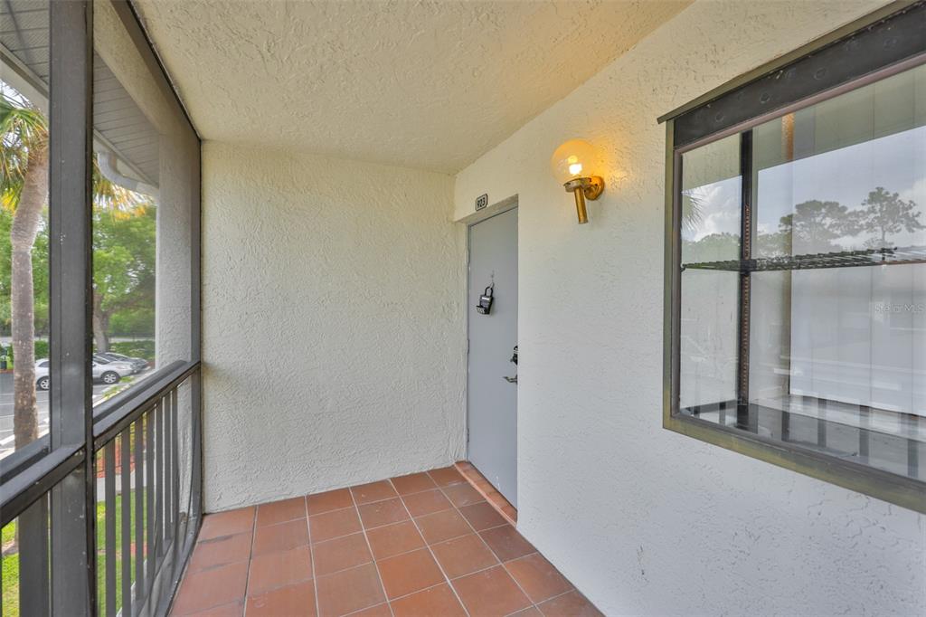 A covered balcony with a tiled floor, a gray entry door, and a screen enclosure — 1934 OYSTER CATCHER STREET UNIT 923, CLEARWATER, FL