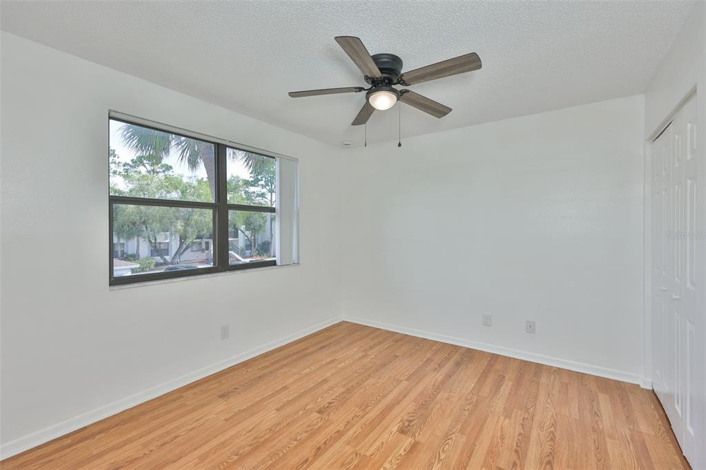 An empty bedroom features white walls, wood-look flooring, a ceiling fan, and a large window — 1934 OYSTER CATCHER STREET UNIT 923, CLEARWATER, FL