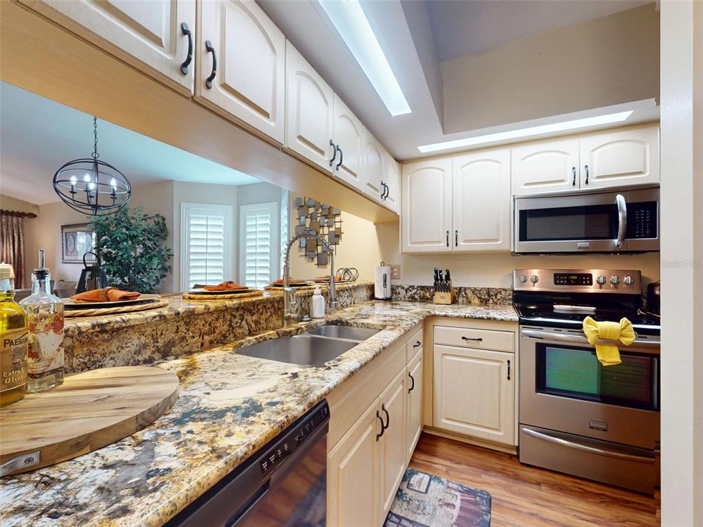 A kitchen features light-colored cabinets, granite countertops, stainless steel appliances, and a pass-through window — 402 BOUCHELLE DRIVE UNIT 206, NEW SMYRNA BEACH, FL
