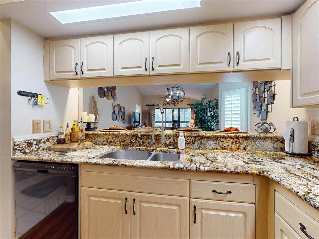 A kitchen with light wood cabinets, granite countertops, and a pass-through window to the living area — 402 BOUCHELLE DRIVE UNIT 206, NEW SMYRNA BEACH, FL