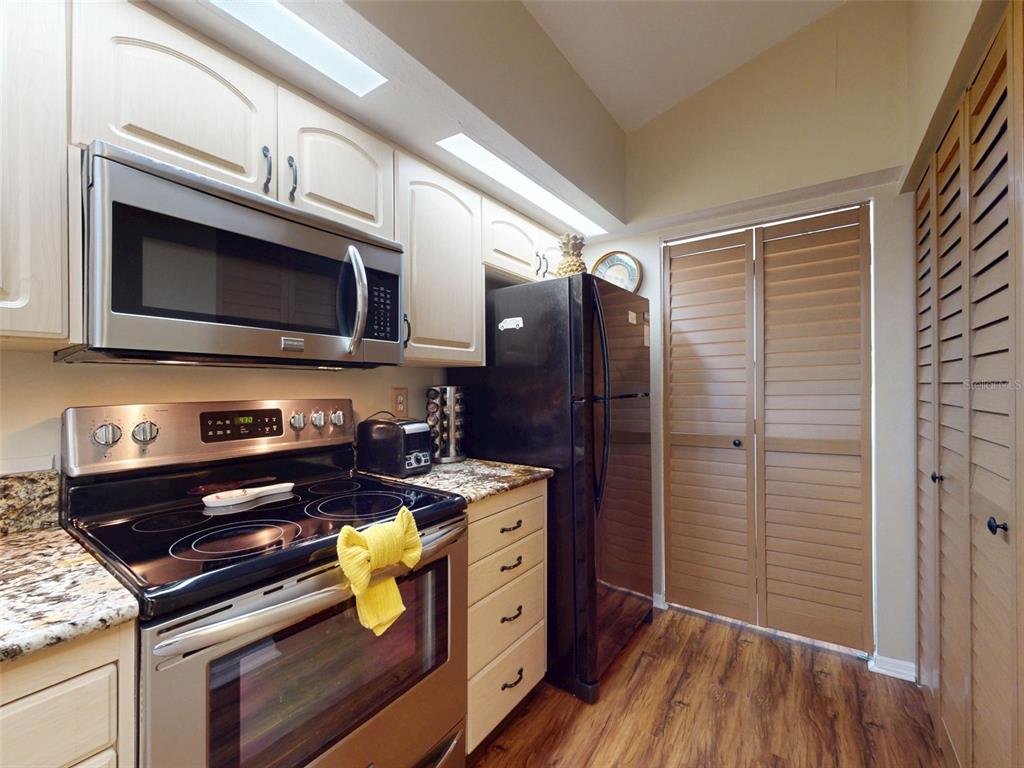 A kitchen features stainless steel appliances, light wood cabinets, granite countertops, and louvered closet doors — 402 BOUCHELLE DRIVE UNIT 206, NEW SMYRNA BEACH, FL