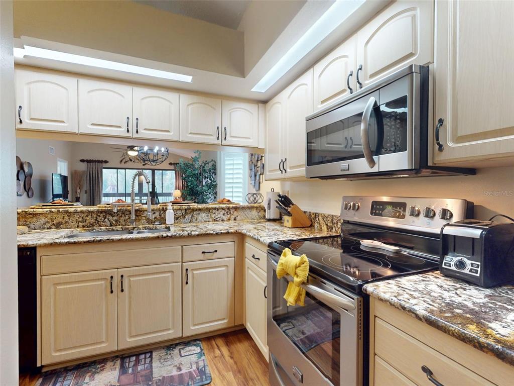 A kitchen features light-colored cabinets, granite countertops, and stainless steel appliances — 402 BOUCHELLE DRIVE UNIT 206, NEW SMYRNA BEACH, FL