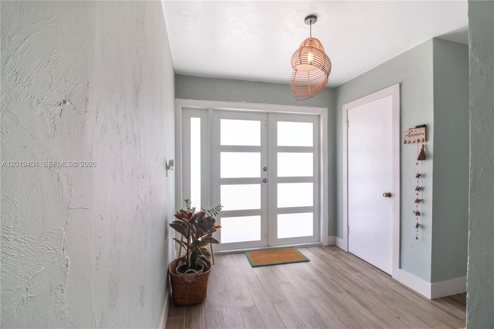 An entryway features light green walls, wood-look flooring, a modern pendant light, and double doors — 10455 SW 200th St, Cutler Bay FL 33157, CUTLER BAY, FL