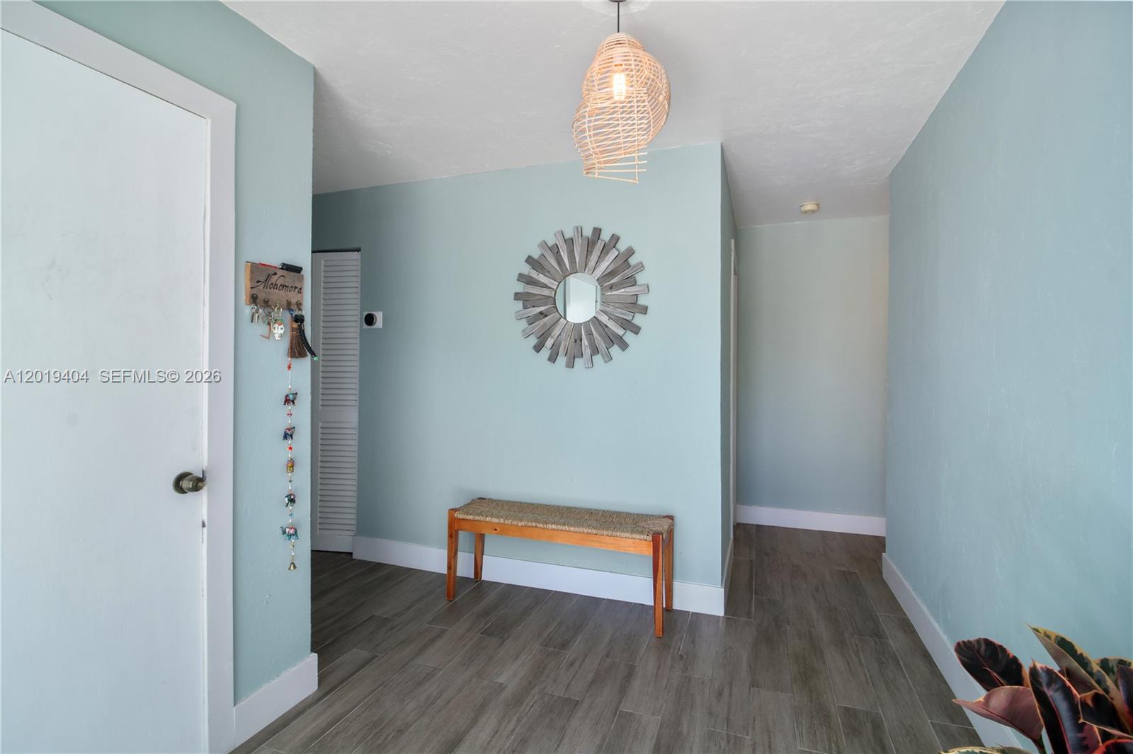 An entryway features light blue walls, a wooden bench, a sunburst mirror, and wood-look flooring — 10455 SW 200th St, Cutler Bay FL 33157, CUTLER BAY, FL