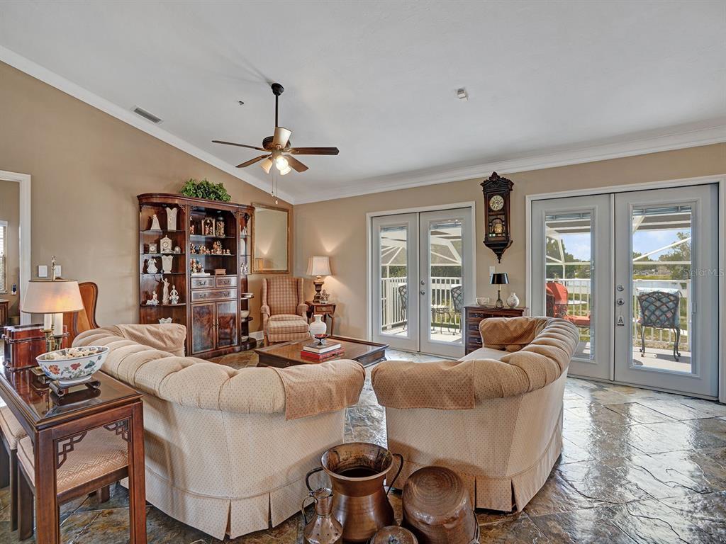 A living room features beige sofas, a wooden hutch, stone flooring, and glass patio doors — 16270 FOREST MIST COURT, ALVA, FL