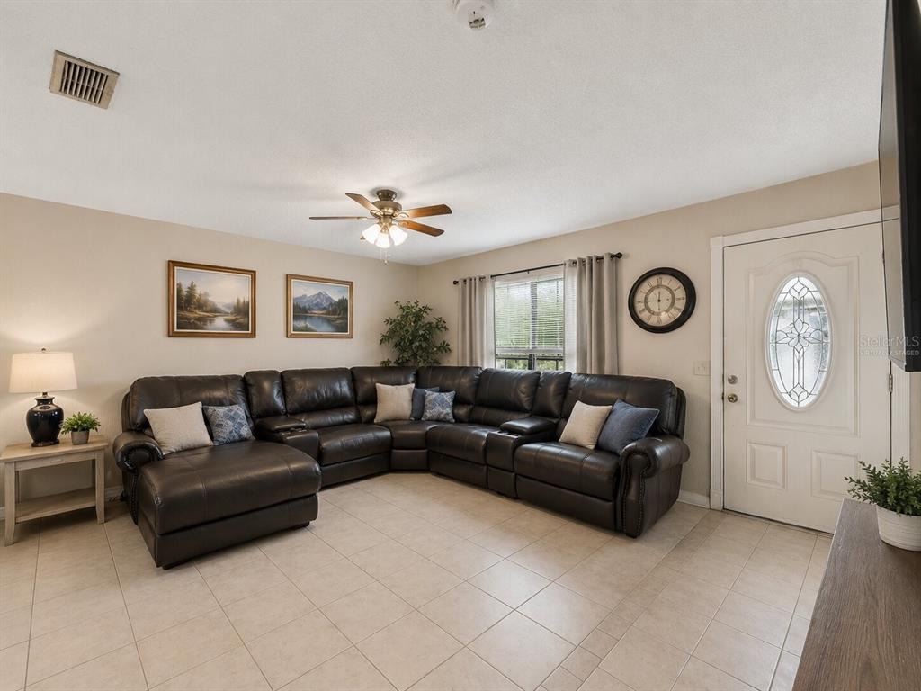 A living room features a large dark leather sectional sofa, tile flooring, and a ceiling fan — 1018 RED BAY TERRACE NW, PORT CHARLOTTE, FL