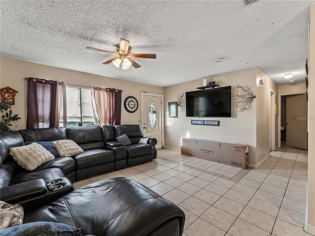 A living room features a large black leather sectional, tiled floors, and a wall-mounted television — 1018 RED BAY TERRACE NW, PORT CHARLOTTE, FL