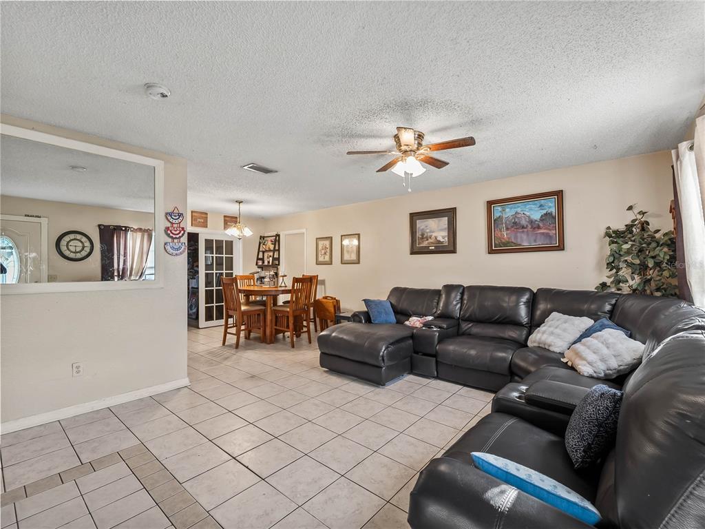 A living room with tile flooring, a large black sectional sofa, and a dining area — 1018 RED BAY TERRACE NW, PORT CHARLOTTE, FL