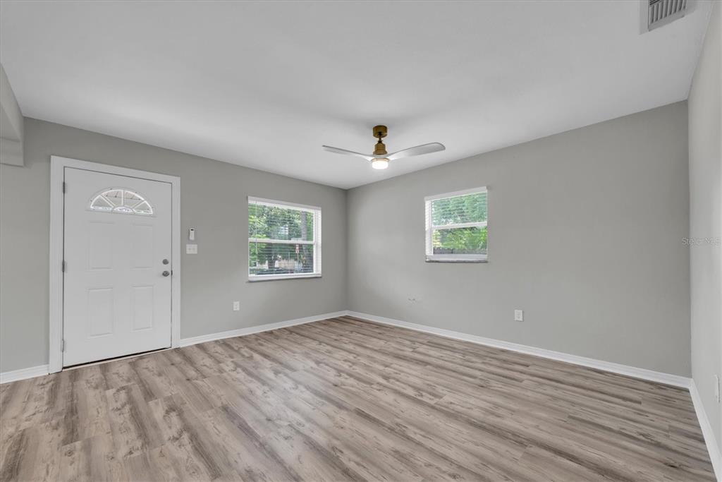 An empty room features gray walls, wood-look flooring, two windows, and a ceiling fan — 1808 S CLUB COURT, TAMPA, FL