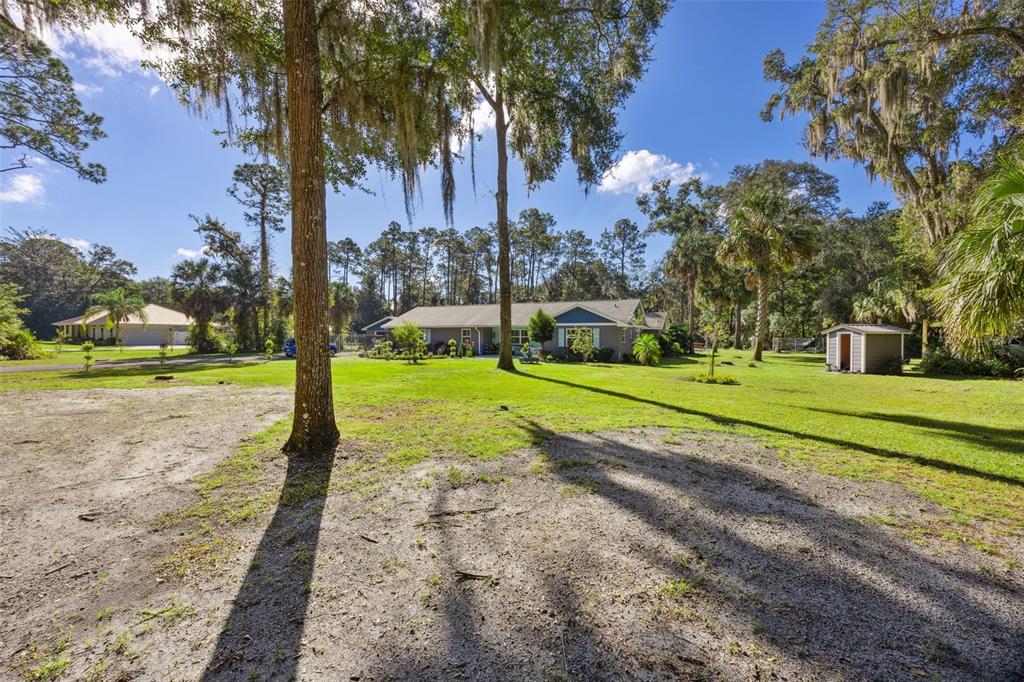 A wide shot of a single-story house with a large lawn and mature trees — 121 HERJA ACRE LANE, PALATKA, FL