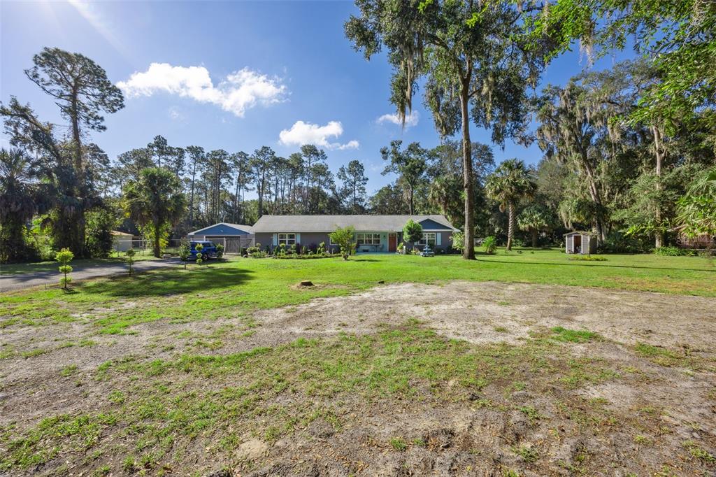 A single-story house with a blue garage sits on a large, grassy, tree-lined lot — 121 HERJA ACRE LANE, PALATKA, FL