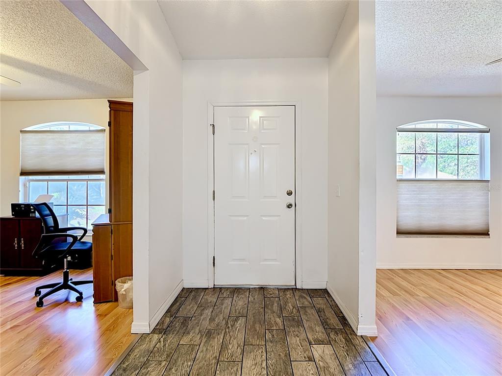 An entryway with a white front door, wood-look tile flooring, and adjacent rooms with wood floors — 2917 EVANS WAY, KISSIMMEE, FL