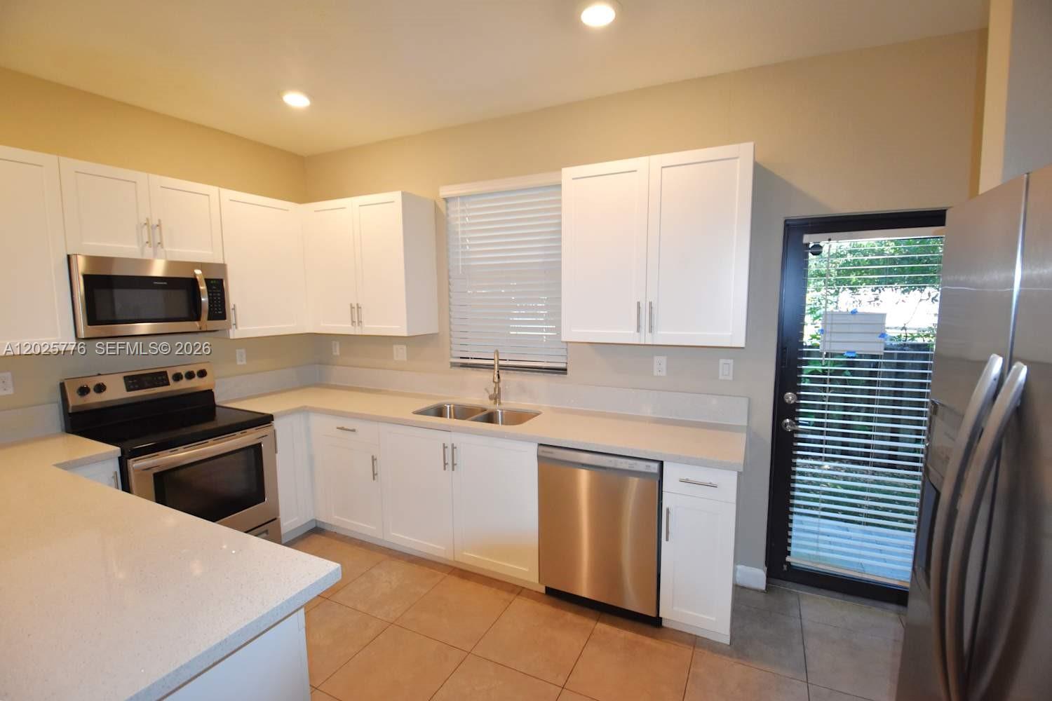 A kitchen features white cabinets, stainless steel appliances, light countertops, and tile flooring — FORT LAUDERDALE, FL