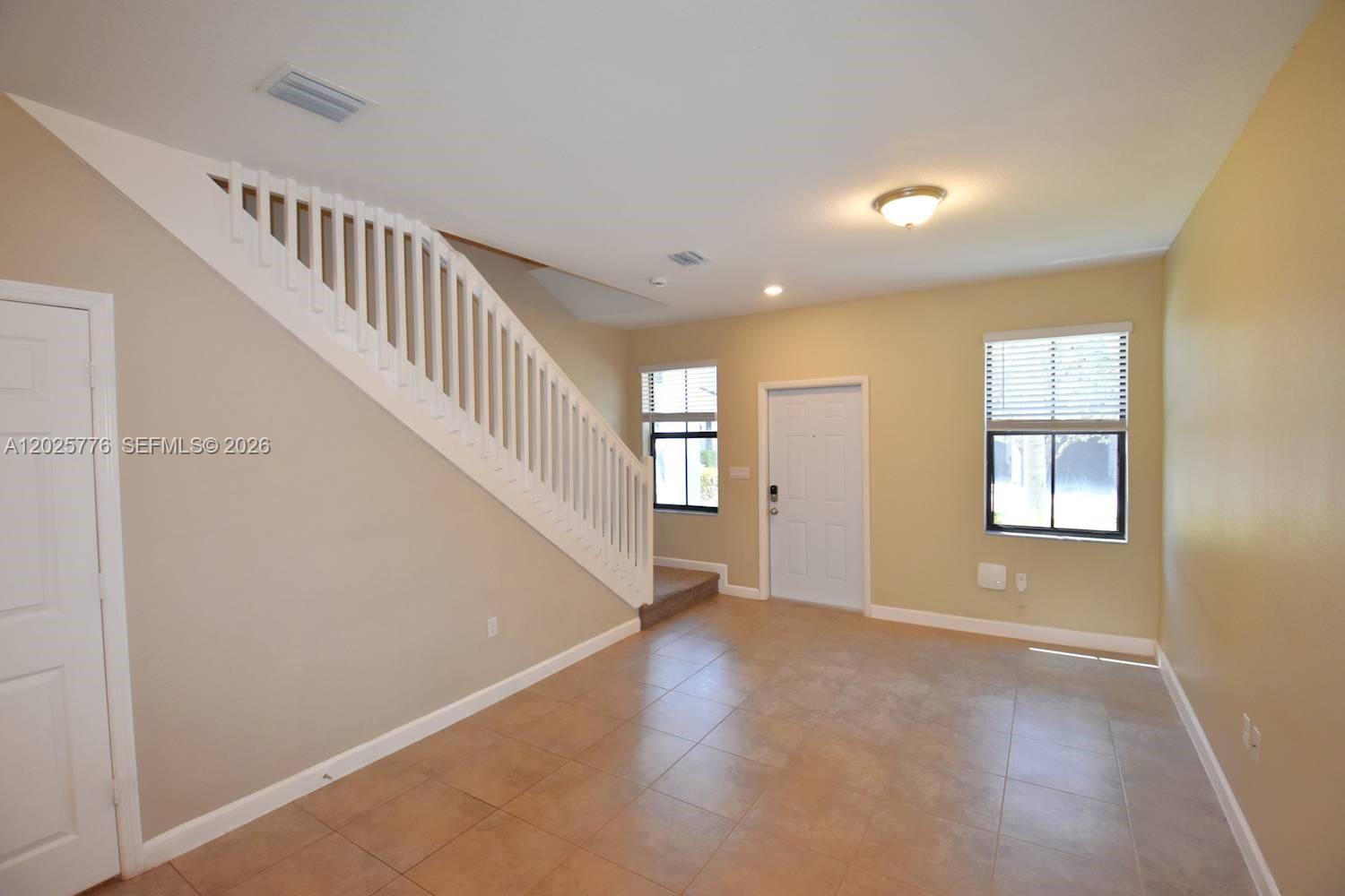 An interior view shows a living area with tiled floors, a staircase, and two windows — FORT LAUDERDALE, FL