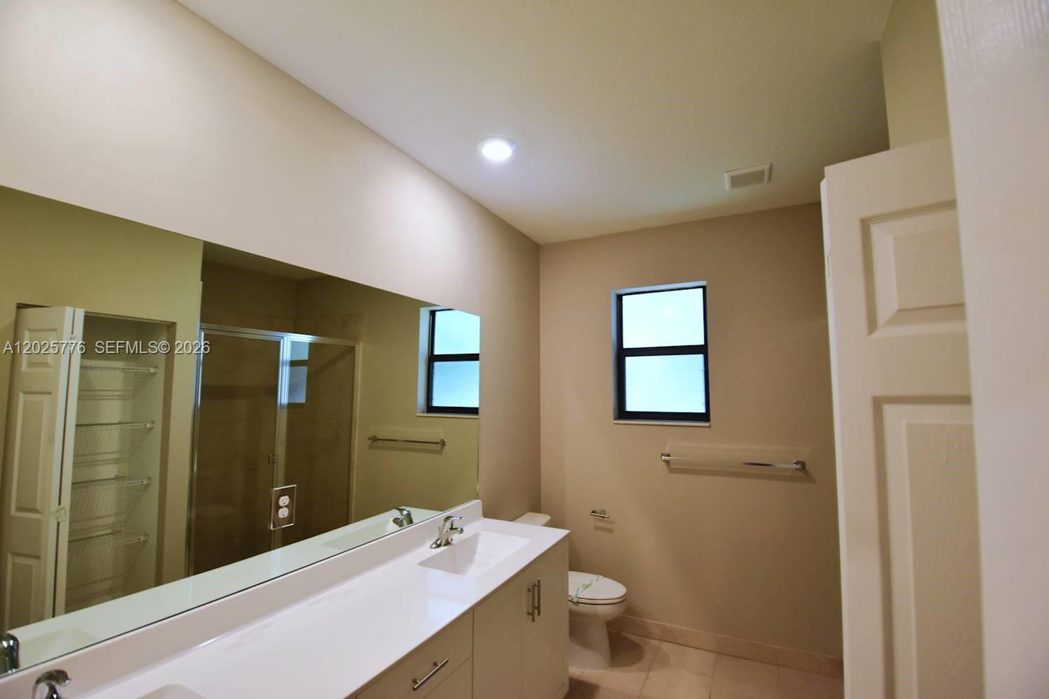 A bathroom features a vanity with a white countertop, a large mirror, and a toilet — FORT LAUDERDALE, FL