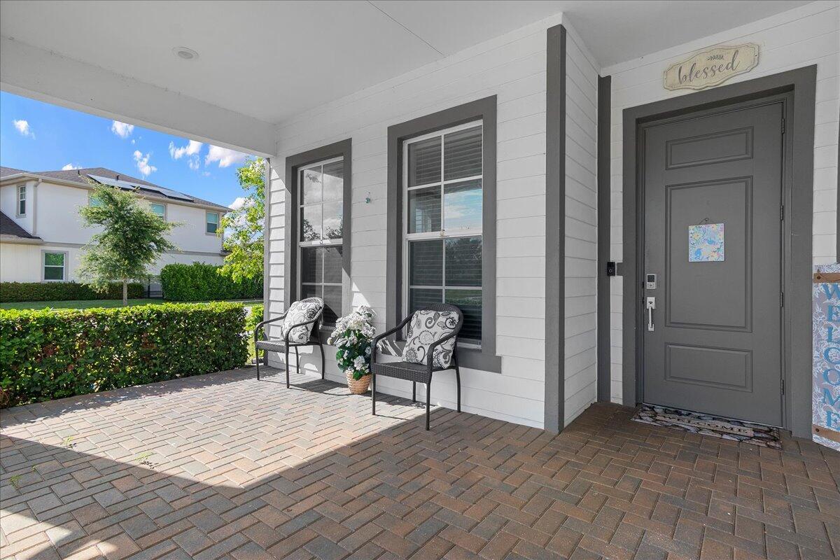 A covered brick porch features two chairs, a gray front door, and white siding — 19656 Tree Stand Terrace, Loxahatchee FL 33470, LOXAHATCHEE, FL