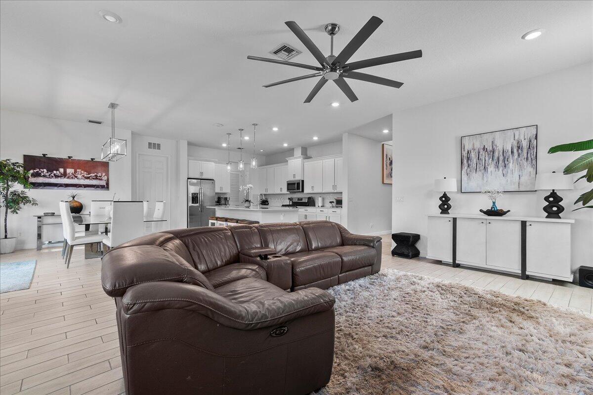 A spacious open-concept living room features a brown leather sectional, shaggy rug, and white kitchen — 19656 Tree Stand Terrace, Loxahatchee FL 33470, LOXAHATCHEE, FL