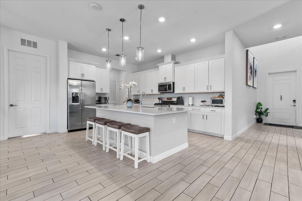 A modern kitchen features white cabinetry, a central island with bar seating, and tile flooring — 19656 Tree Stand Terrace, Loxahatchee FL 33470, LOXAHATCHEE, FL