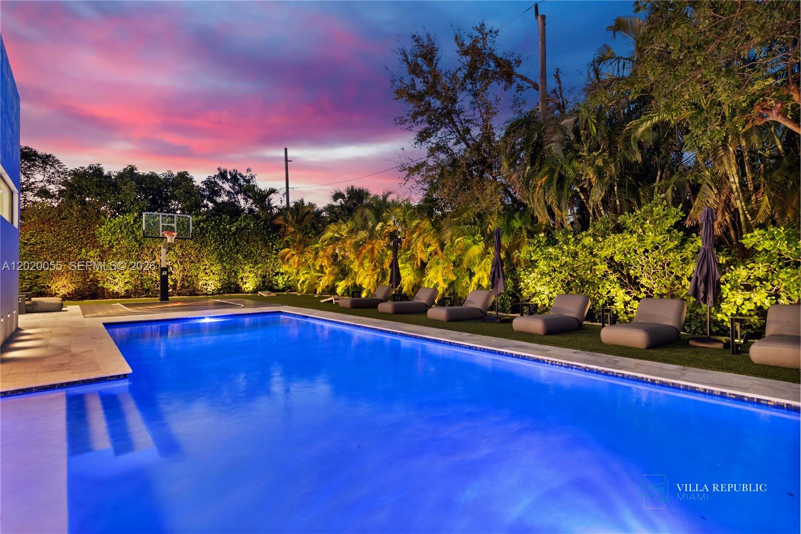 A swimming pool with lounge chairs and a basketball hoop at sunset — 1941 NE 196th Ter, Miami FL 33179, MIAMI, FL