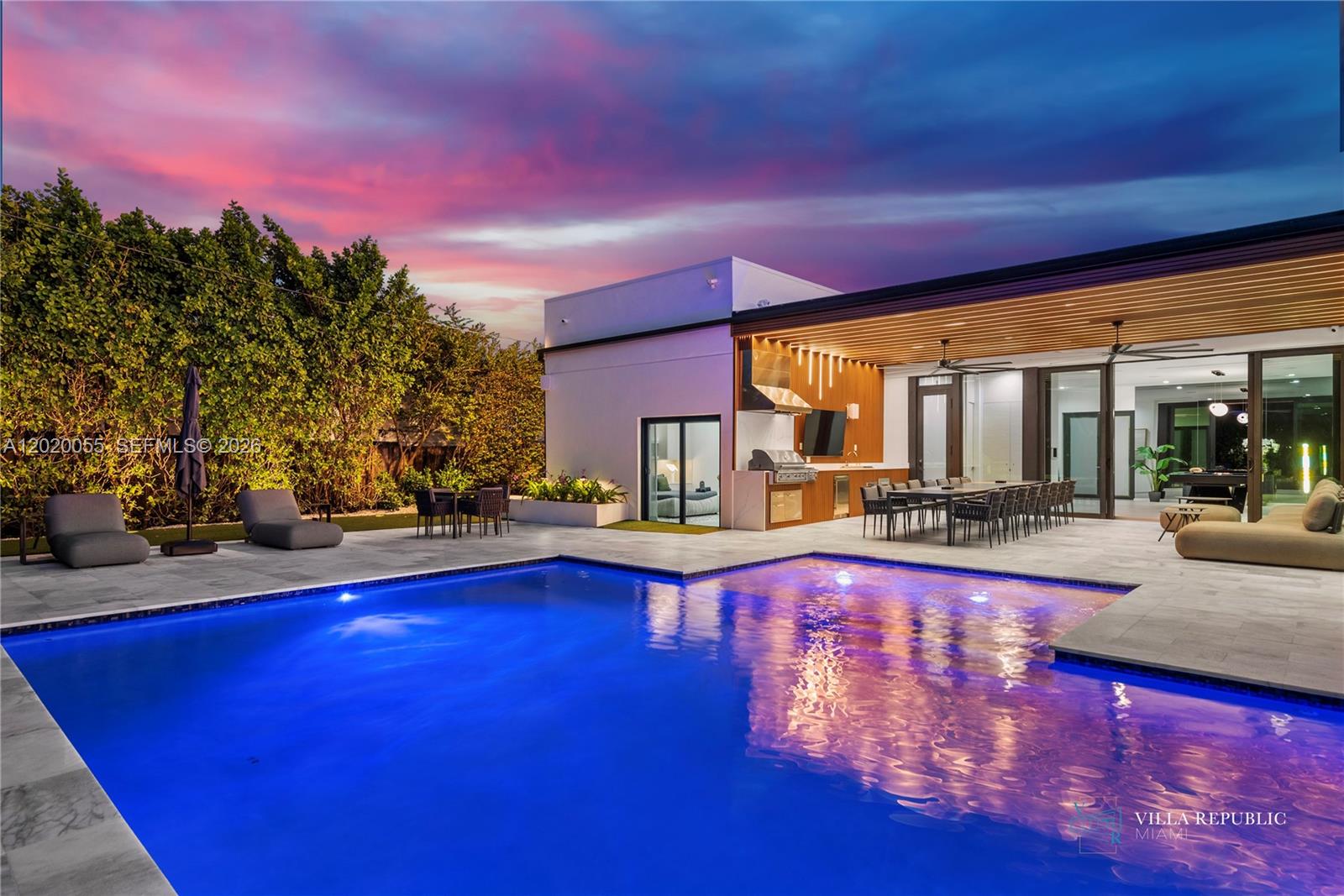 A modern outdoor patio features a swimming pool, dining area, and kitchen under a pergola — 1941 NE 196th Ter, Miami FL 33179, MIAMI, FL