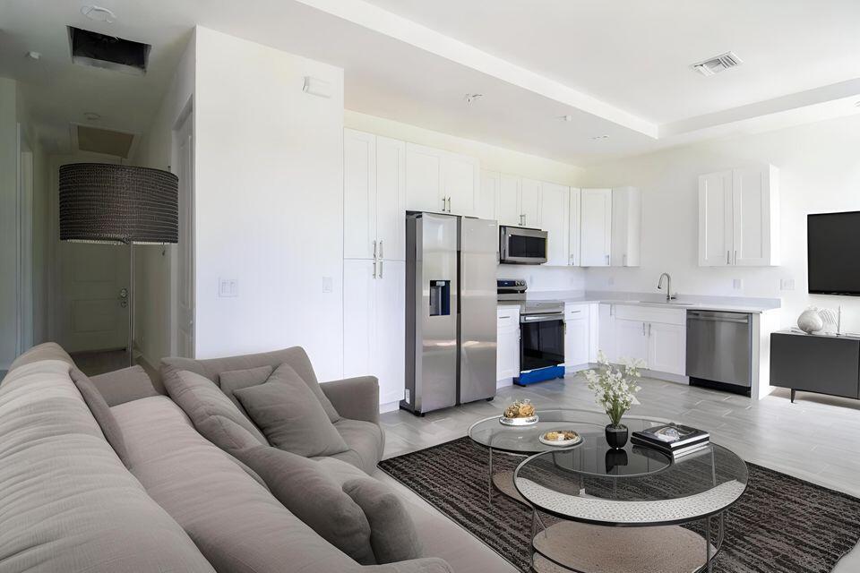 A modern open-concept kitchen and living area features white cabinetry, stainless steel appliances, and gray furniture — 260 Rotonda Boulevard # 2, FL 33947, FL