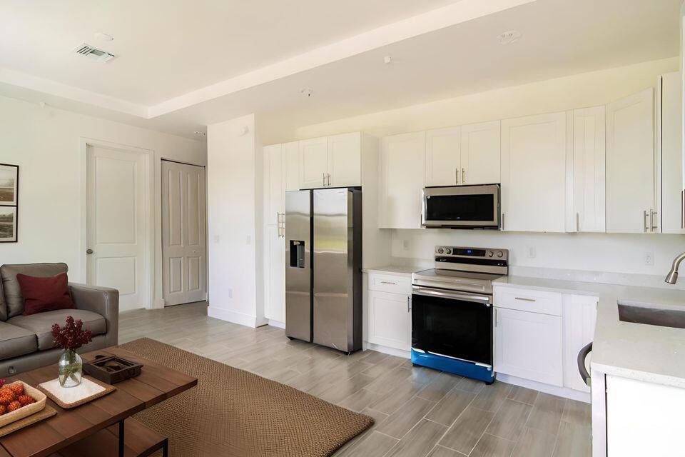 A kitchen with white cabinets and stainless steel appliances opens into a living room area — 260 Rotonda Boulevard # 2, FL 33947, FL
