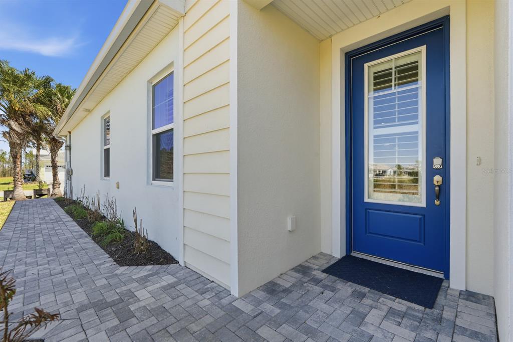 A blue front door with a glass insert sits on a paved walkway beside a house — 896 CORAL REEF WAY, DAYTONA BEACH, FL