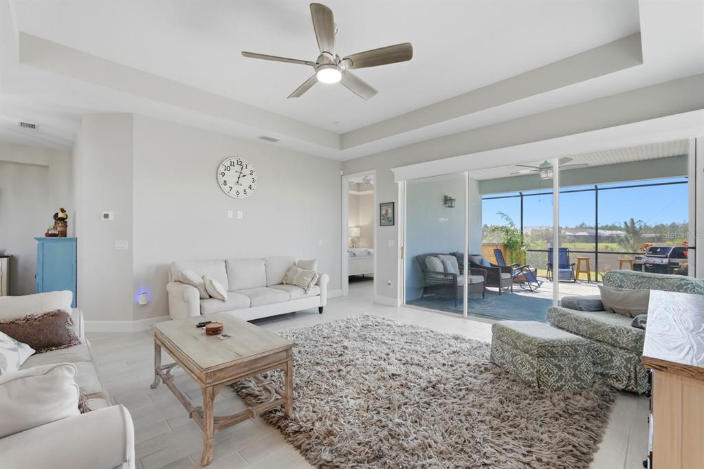 A living room with a tray ceiling, white sofa, patterned armchair, and sliding glass doors — 896 CORAL REEF WAY, DAYTONA BEACH, FL