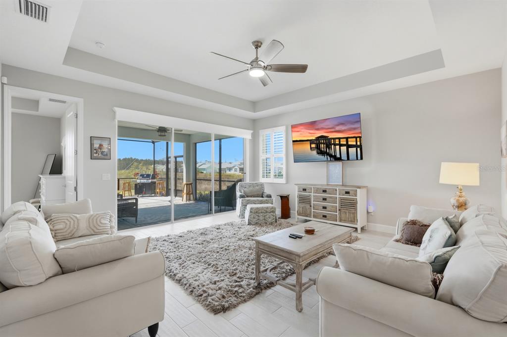 A living room features a tray ceiling, light tile floors, and sliding doors to a patio — 896 CORAL REEF WAY, DAYTONA BEACH, FL
