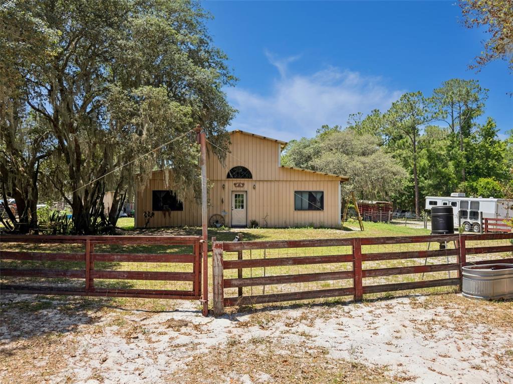 A tan metal-sided house sits behind a red wooden fence on a sandy lot — BLUE JAY WAY, DAVENPORT, FL