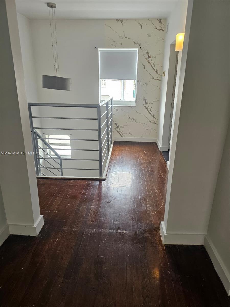A hallway with dark wood flooring leads to a staircase with a metal railing — 1614 Jefferson Ave # 3, Miami Beach FL 33139, MIAMI BEACH, FL