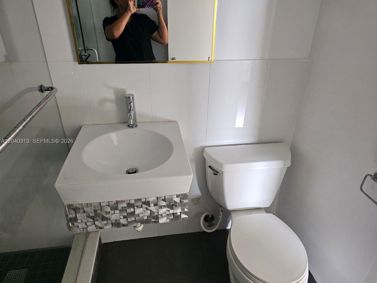 A bathroom features a wall-mounted sink with a decorative tiled base and a white toilet — 1614 Jefferson Ave # 3, Miami Beach FL 33139, MIAMI BEACH, FL