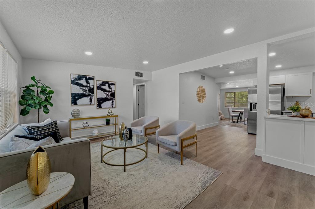 A living room with light wood floors, two armchairs, a sofa, and an open kitchen — 849 LOGAN DRIVE, LONGWOOD, FL