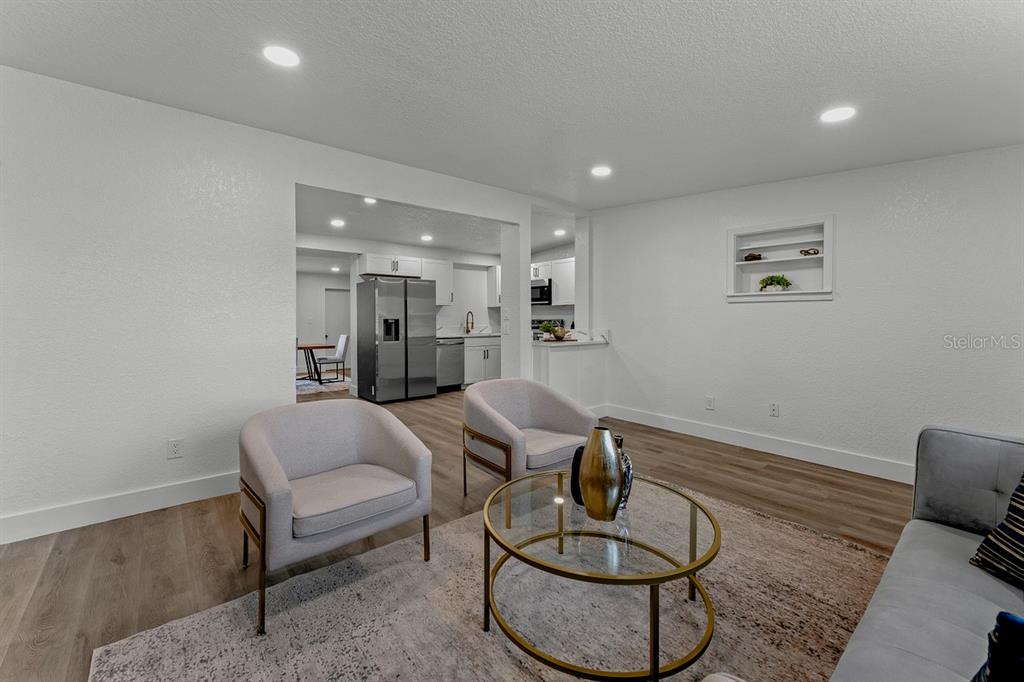 A living room with two armchairs, a glass coffee table, and an open kitchen beyond — 849 LOGAN DRIVE, LONGWOOD, FL