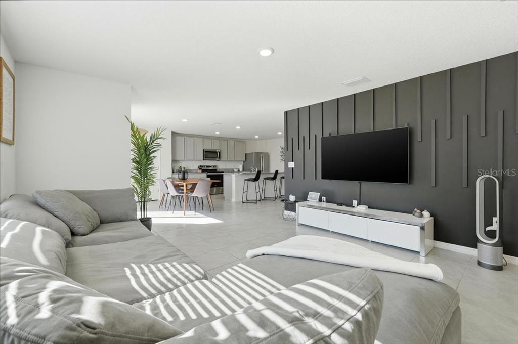 A living room with a gray sectional sofa, a dark accent wall, and an open kitchen — 1211 TAHITIAN SUNRISE DRIVE, PLANT CITY, FL