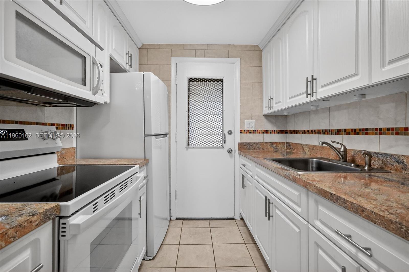 A galley kitchen features white cabinets, granite countertops, a white refrigerator, and a rear door — 16901 NE 13th Ave # 108, Miami FL 33162, MIAMI, FL