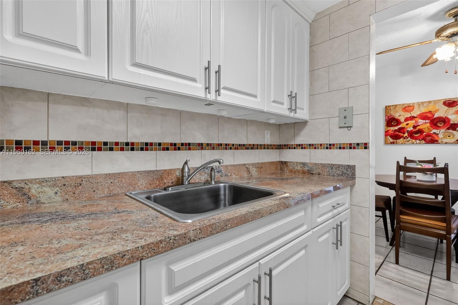 A kitchen features white cabinets, granite countertops, a stainless steel sink, and a tiled backsplash — 16901 NE 13th Ave # 108, Miami FL 33162, MIAMI, FL