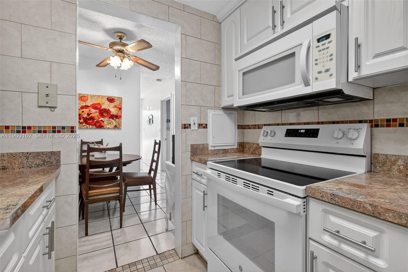 A kitchen with white cabinets, granite countertops, and a white stove leads into a dining area — 16901 NE 13th Ave # 108, Miami FL 33162, MIAMI, FL
