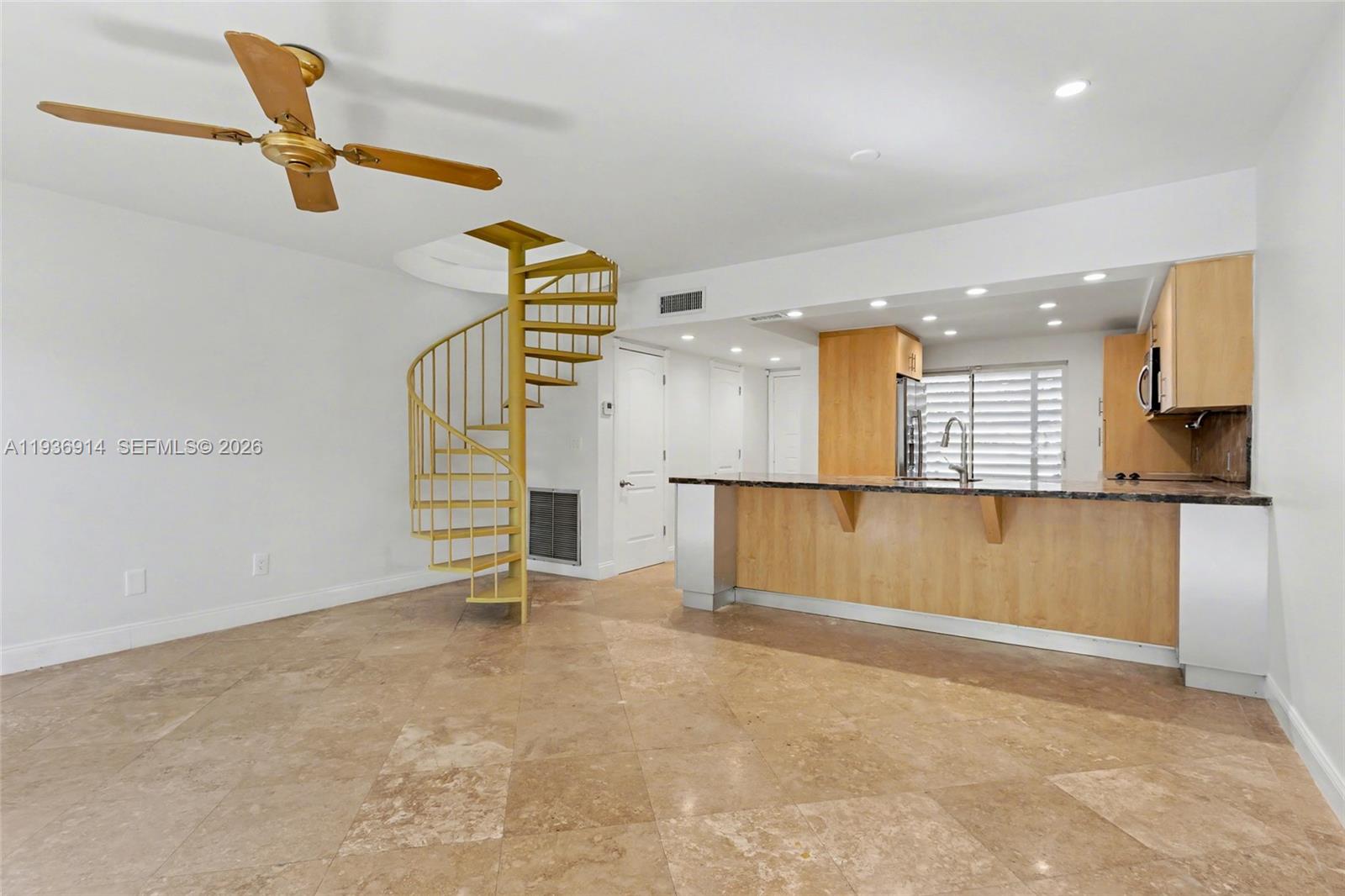 A room with tile floors, a spiral staircase, and an open kitchen with wooden cabinets — 523 NE 38th St # 6, Miami FL 33137, MIAMI, FL