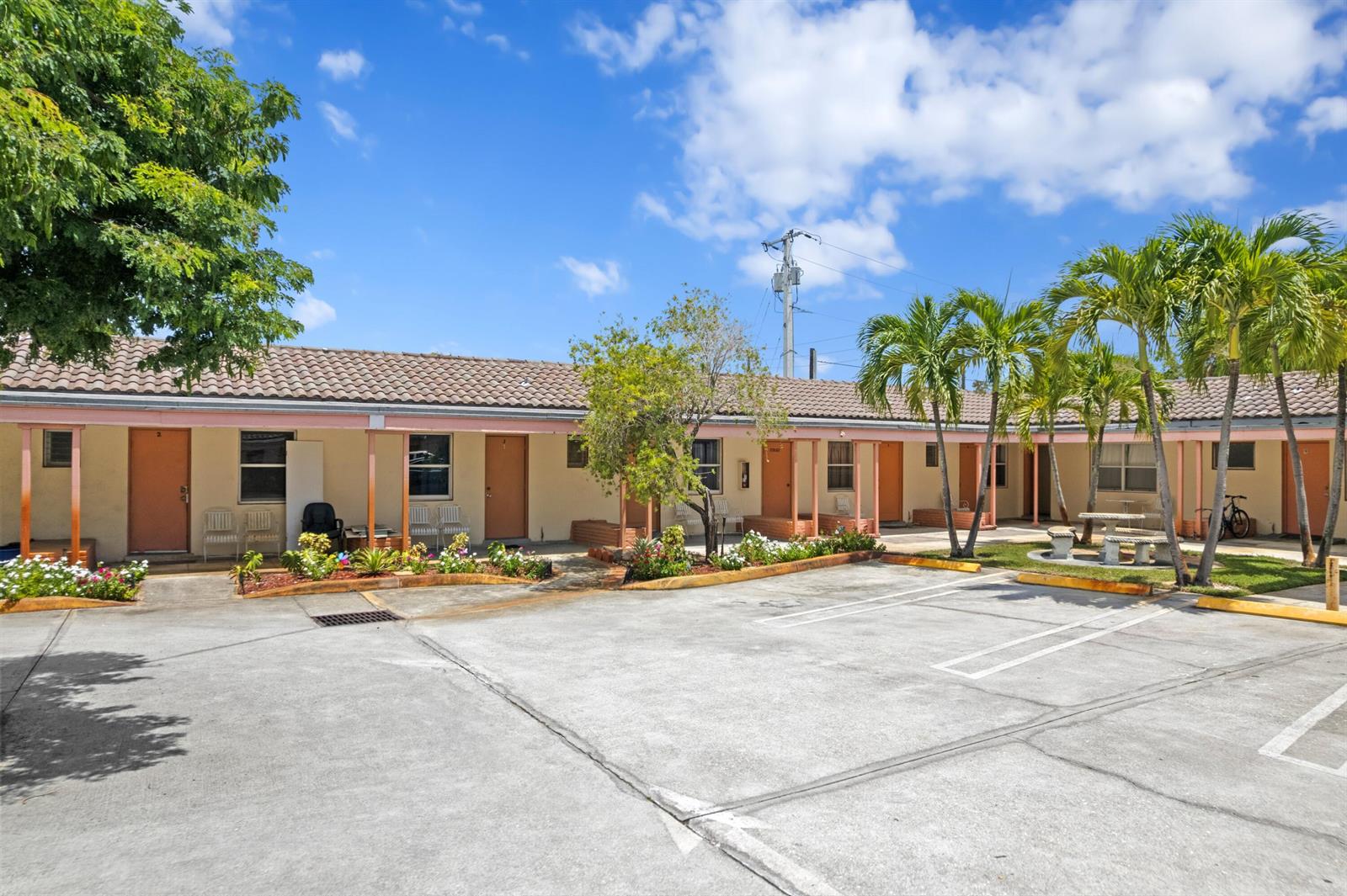 A single-story motel building with a concrete parking lot and palm trees under a blue sky — 7800 S Dixie Highway, West Palm Beach FL 33405, WEST PALM BEACH, FL