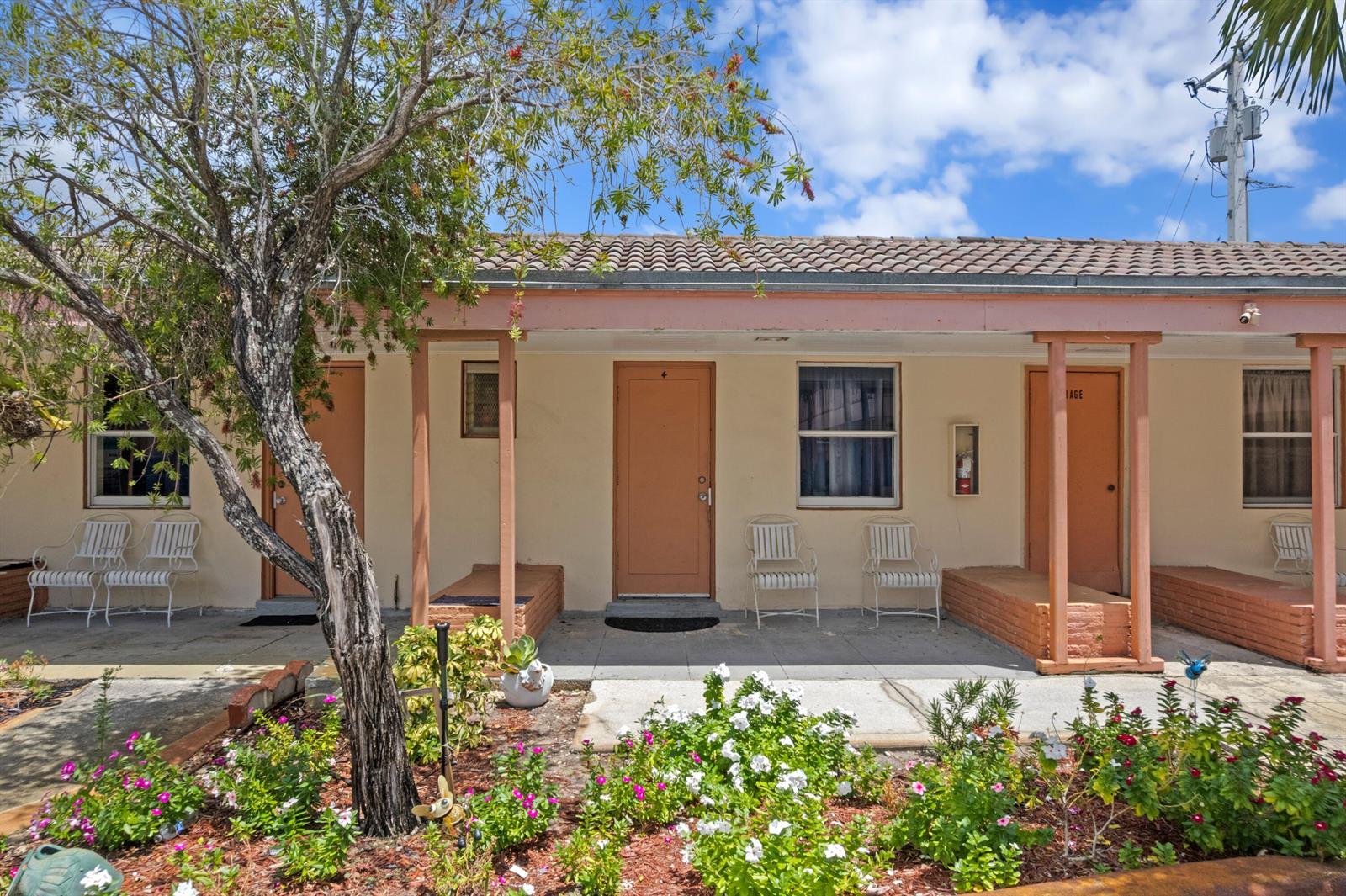 A row of motel-style rooms with orange doors, white chairs, and a front garden — 7800 S Dixie Highway, West Palm Beach FL 33405, WEST PALM BEACH, FL