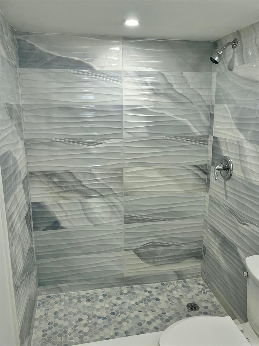A shower stall features wavy, gray-toned wall tiles and a small, hexagonal mosaic floor — 3201 NE 8th Street # 206, Pompano Beach FL 33062, POMPANO BEACH, FL