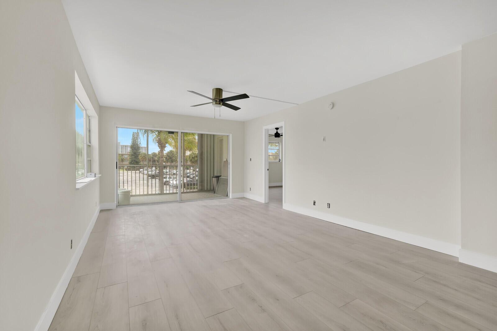 An empty living room features light wood-look flooring, a ceiling fan, and sliding glass doors — 3201 NE 8th Street # 206, Pompano Beach FL 33062, POMPANO BEACH, FL