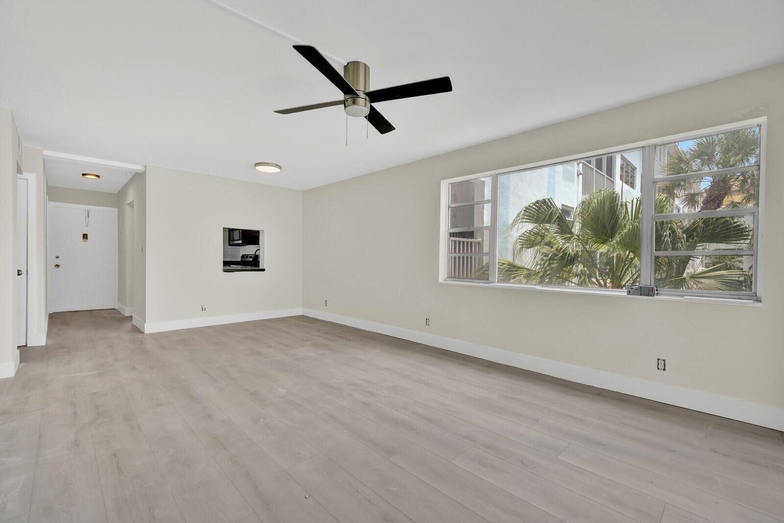 An empty living room with light wood-look flooring, a ceiling fan, and a large window — 3201 NE 8th Street # 206, Pompano Beach FL 33062, POMPANO BEACH, FL