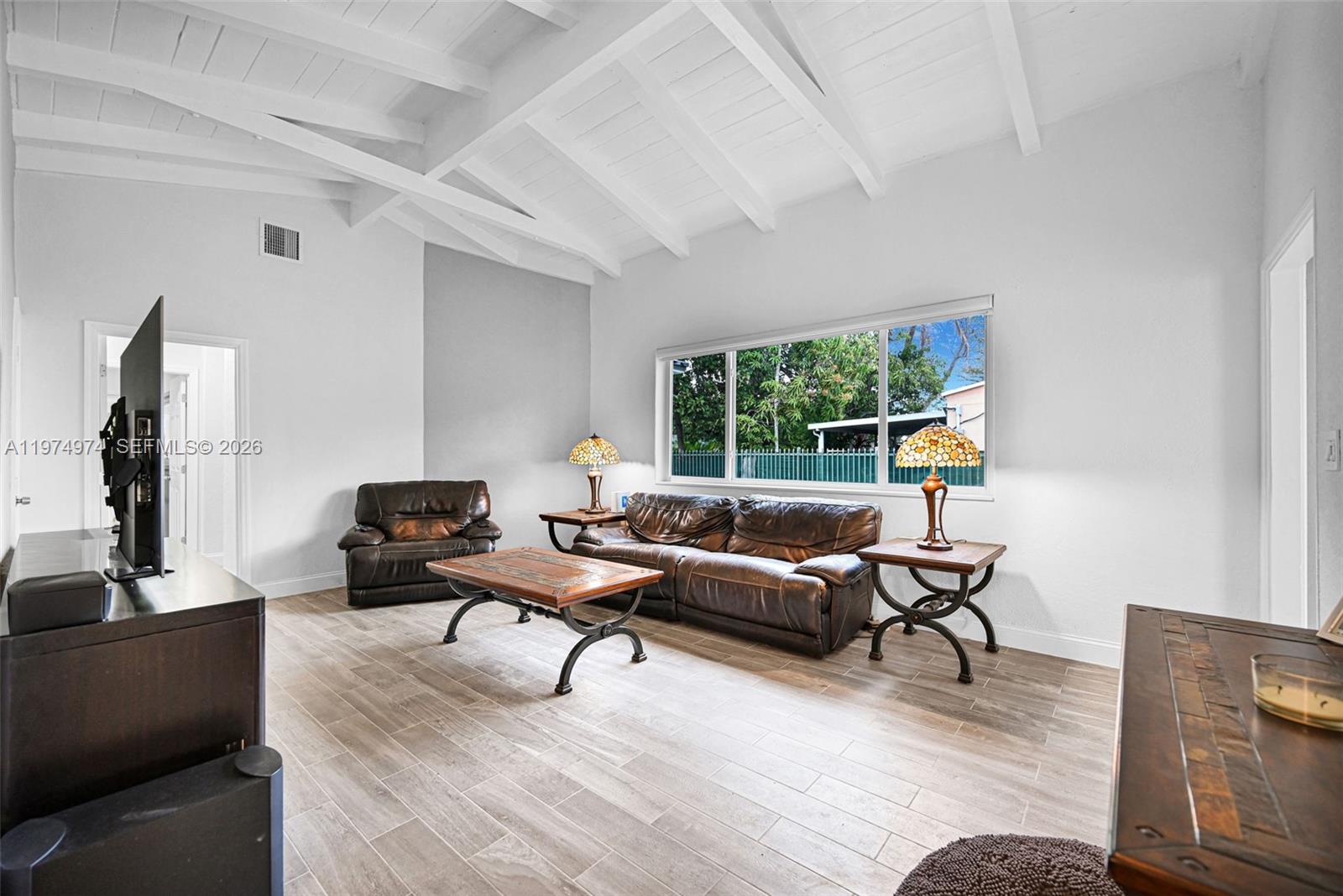 A living room features a vaulted ceiling, brown leather furniture, and wood-look tile flooring — 1021 NE 82nd Ter, Miami FL 33138, MIAMI, FL