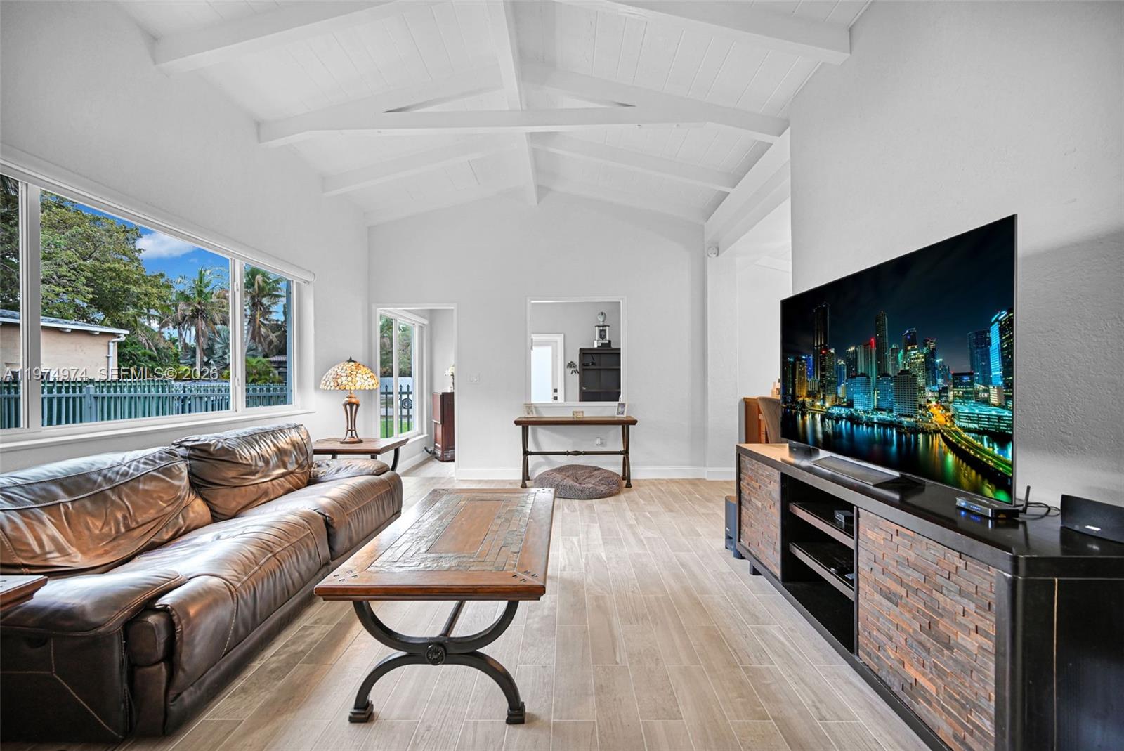 A living room features a vaulted ceiling, wood-look tile floors, a leather sofa, and television — 1021 NE 82nd Ter, Miami FL 33138, MIAMI, FL